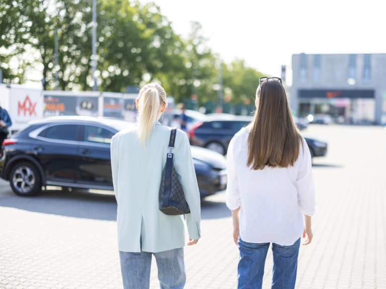 To kvinder går gennem en parkeringsplads med synlige Freetrailer-trailere i baggrunden – illustrerer den daglige eksponering ved at blive partner.