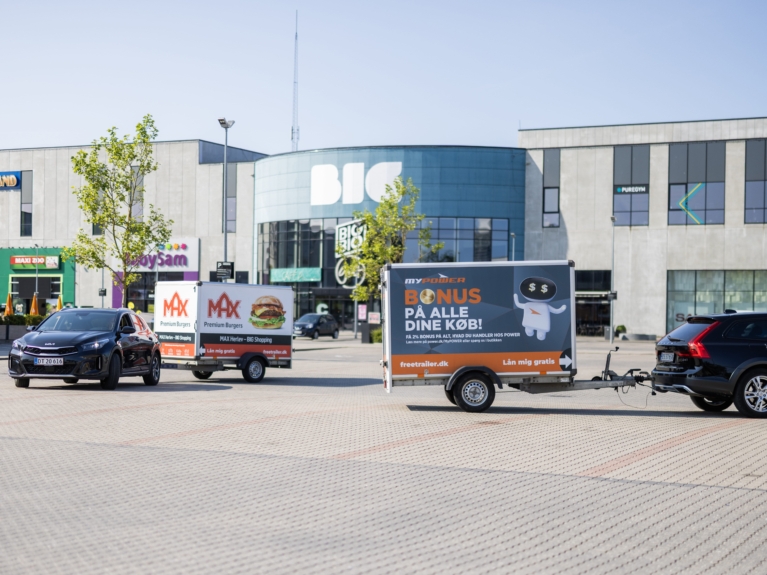 Two cars pulling branded Freetrailer trailers in front of the BIG Shopping center in Herlev, Denmarkâ€”one promoting MAX Burgers and the other POWER. A visual example of how businesses can increase exposure and foot traffic through branded trailers.