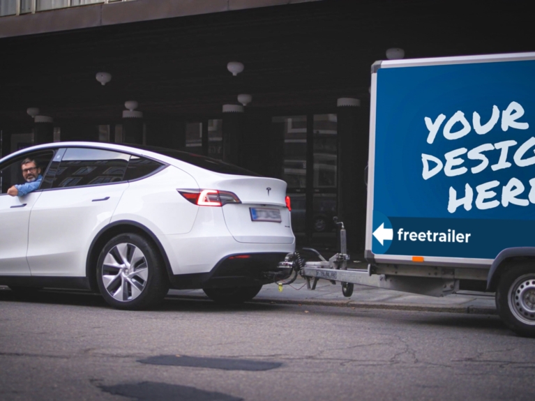 Hvid Tesla trækker Freetrailer med teksten “Your design here” – viser det store reklamepotentiale ved at blive partner.